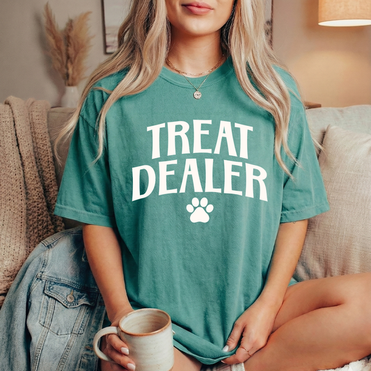Person wearing a teal t-shirt with 'Treat Dealer' text and holding a mug.